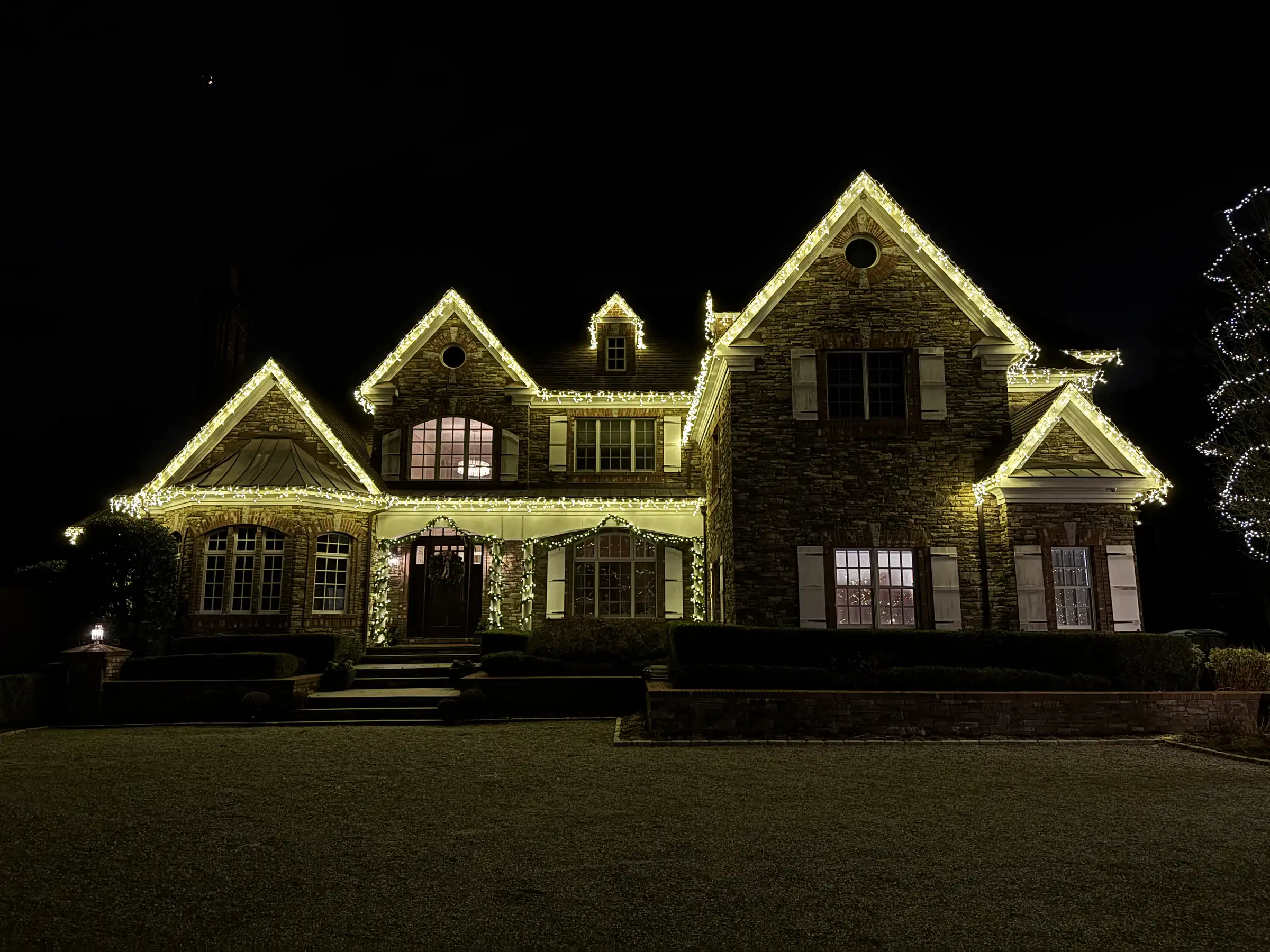 Warm white Christmas lights outlining a stone home at night